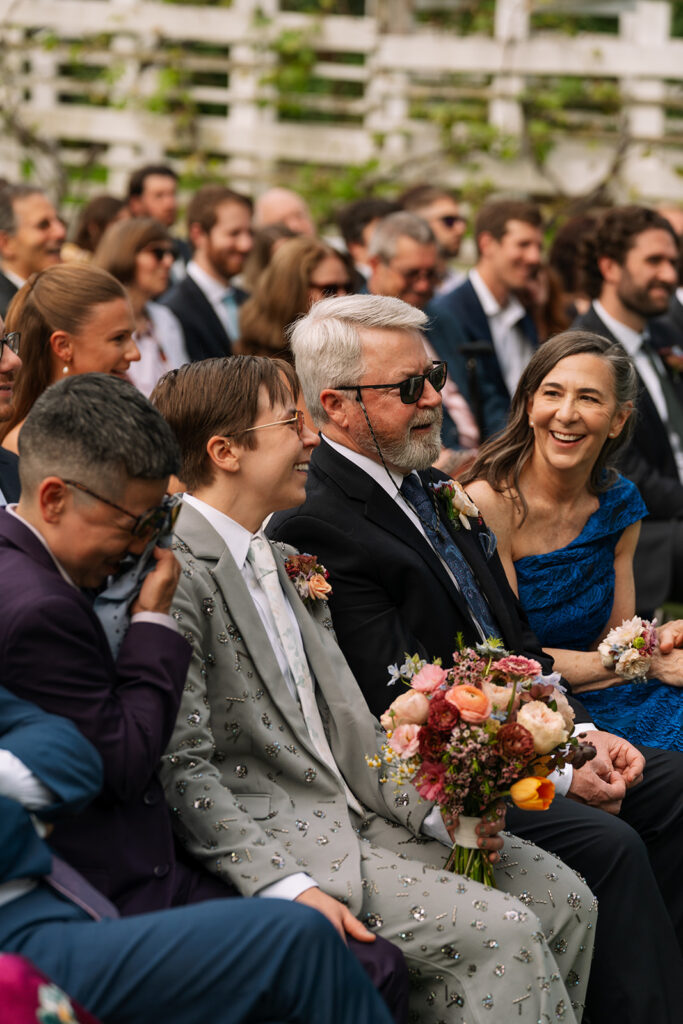 Ceremony guests seated on white chairs, floral aisle arrangements blooming in the foreground.