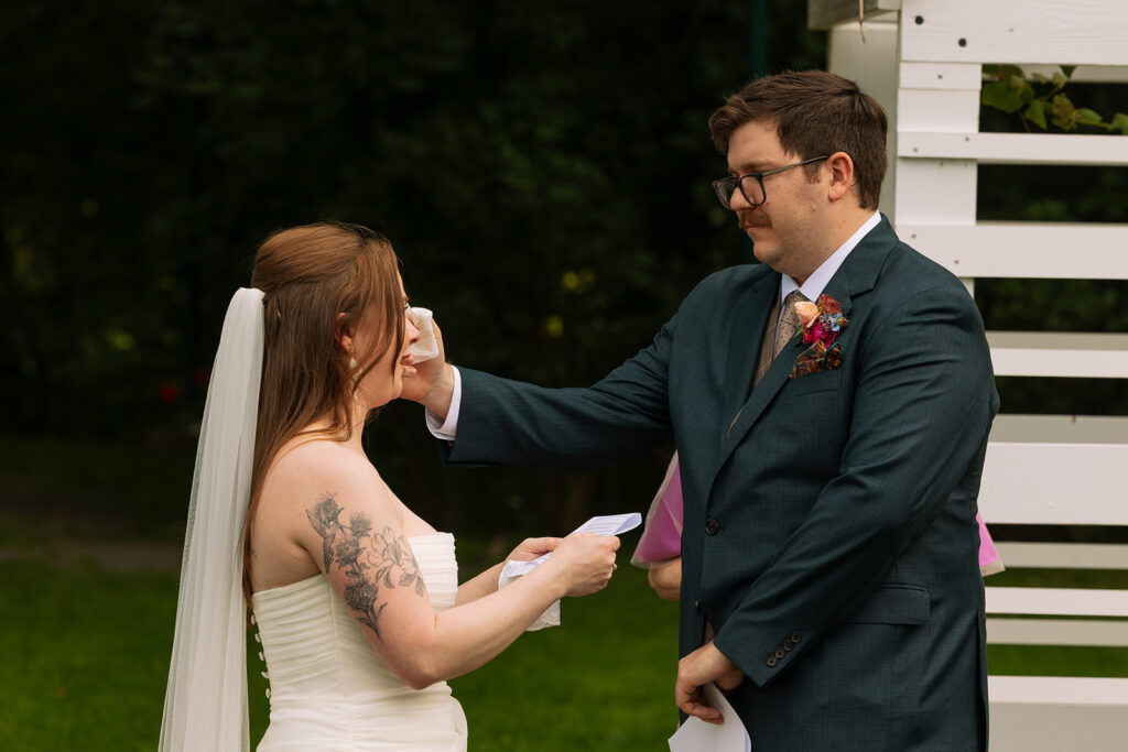 Bride wiping away tears while exchanging vows with the groom.
