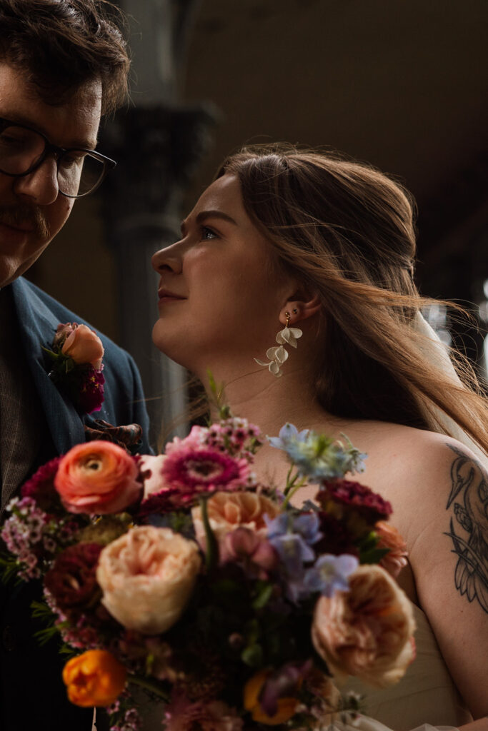 Bride holding colorful bouquet, leaning in close to her partner with soft smiles.