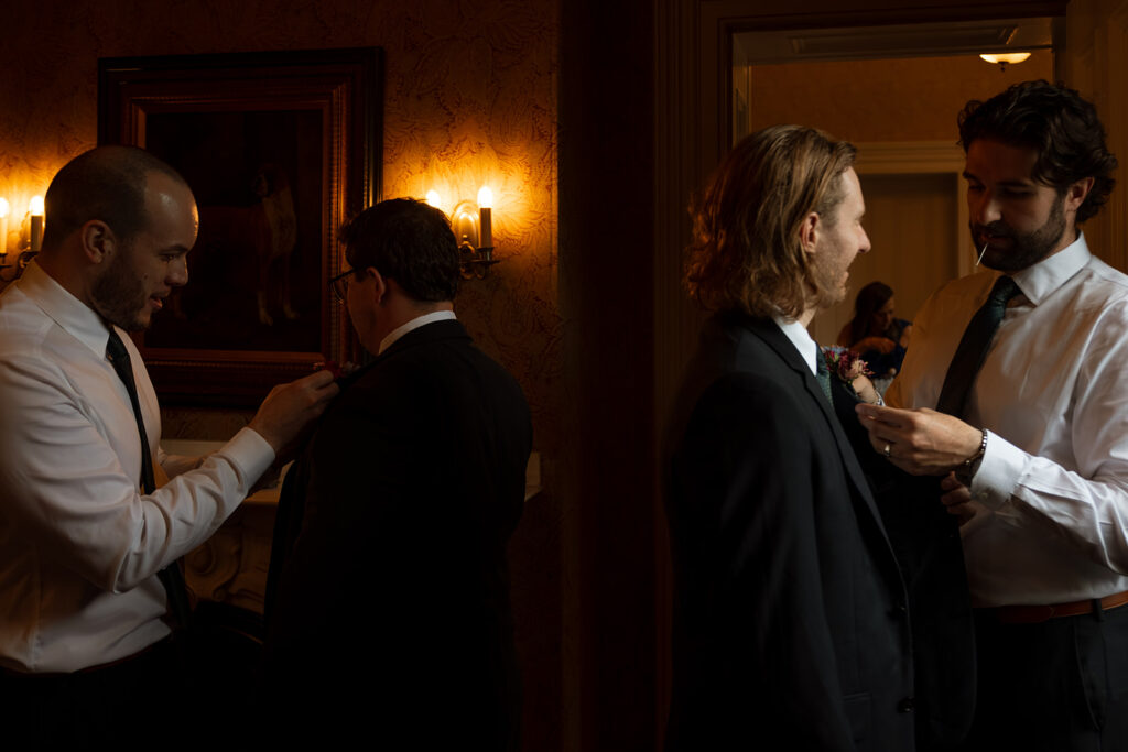 Groom and groomsmen adjusting boutonnieres, caught in an intimate candid moment.