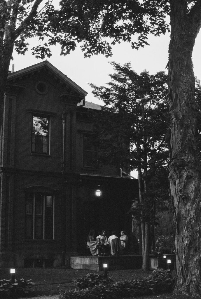 Film wedding photography of exterior of Commander’s Mansion at dusk, guests gathered outside under the trees.