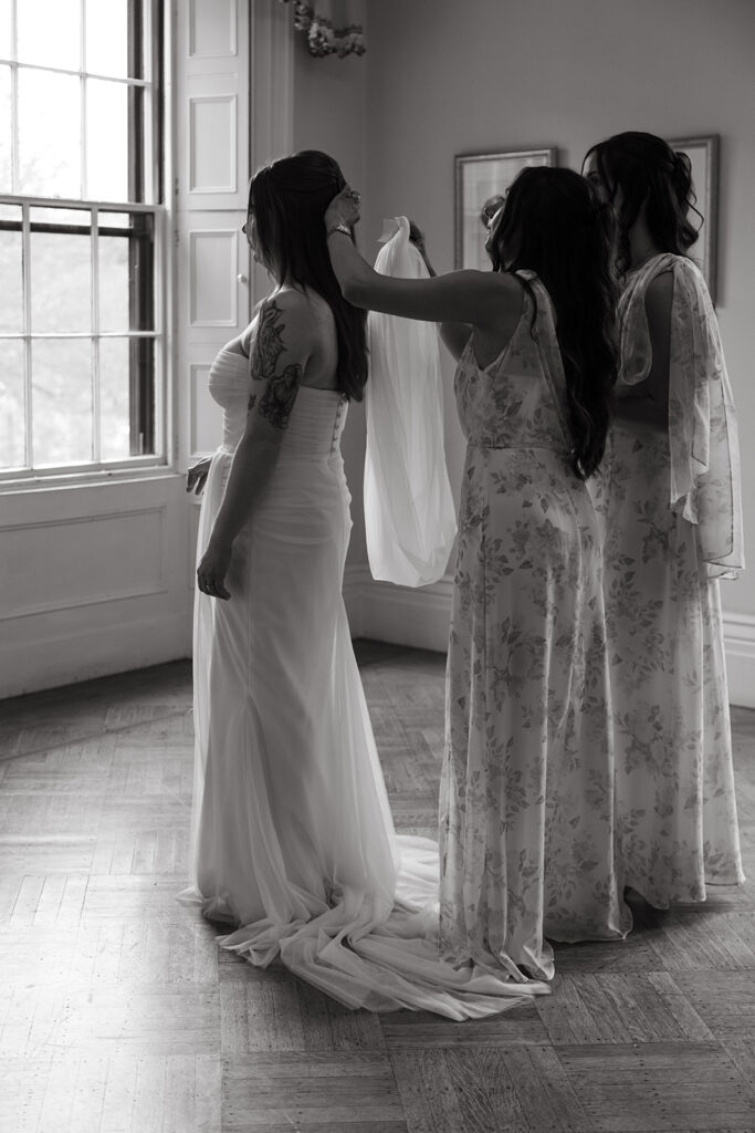 Bride with bridesmaids in front of a tall window, natural light glowing across the scene.