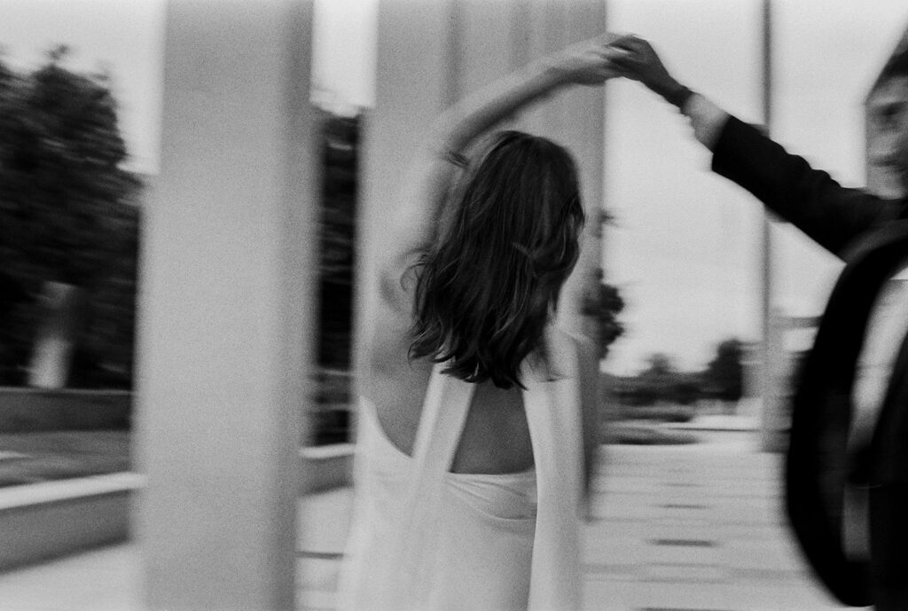 Motion blur shot of the bride twirling with groom’s hand, documentary-style engagement photography in black and white.