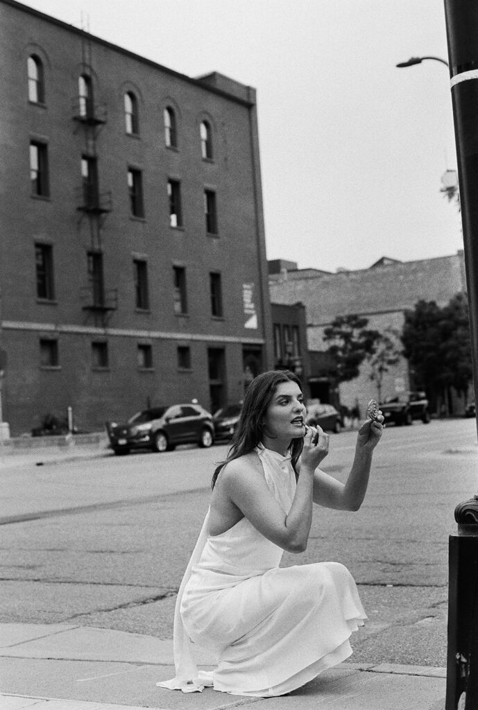 Bride crouching on Minneapolis streets, silk gown pooling at her feet, cinematic black-and-white shot.
