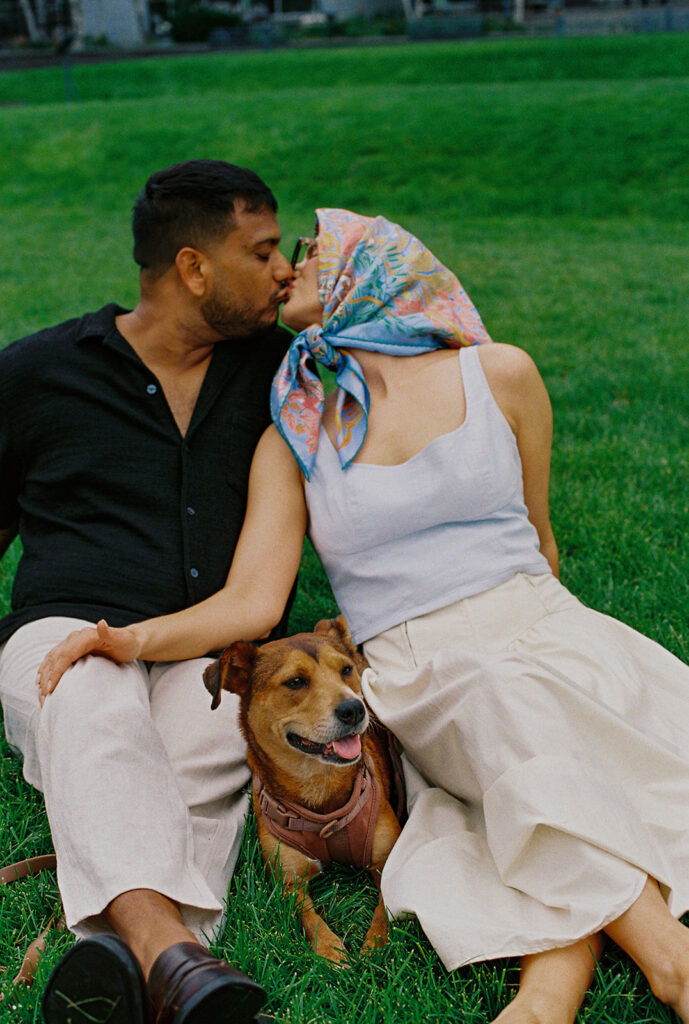 Couple kissing with dog between them, joyful chaos during documentary engagement photos in Twin Cities