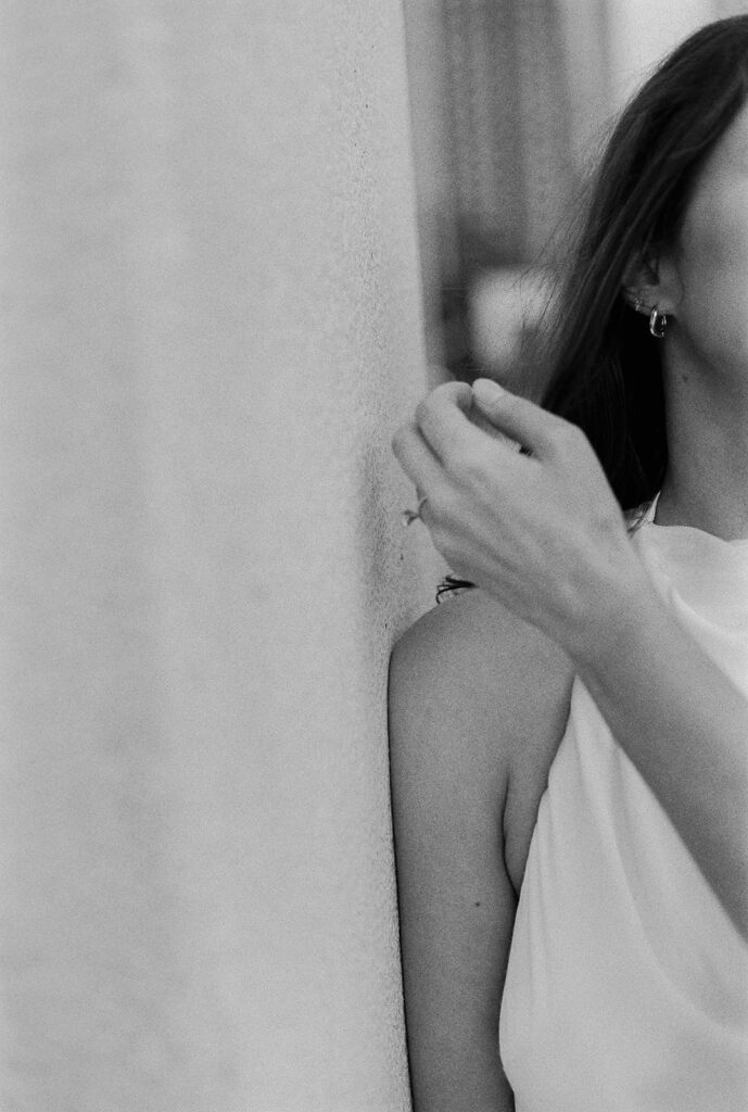 Bride leaning against concrete pillar, minimalistic portrait in black-and-white film.