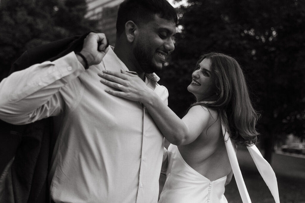 Groom slipping on jacket while fiancée smiles at him, downtown Minneapolis.
