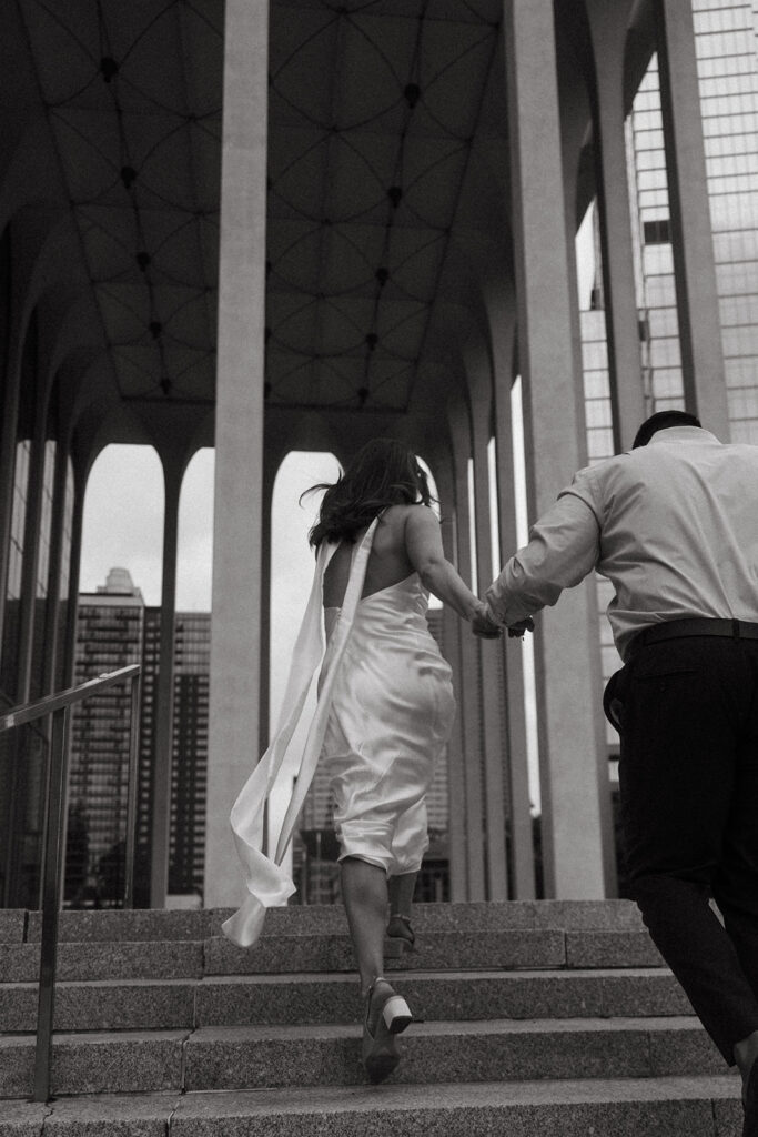 Couple ascending stone steps at the Northwestern National Life Building, flowing white dress trailing behind.