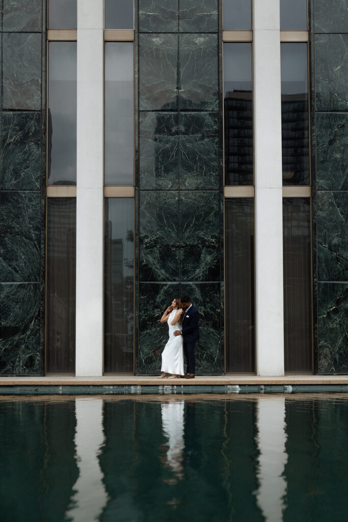 Couple framed against reflective glass façade with fountain pool in Minneapolis engagement photography
