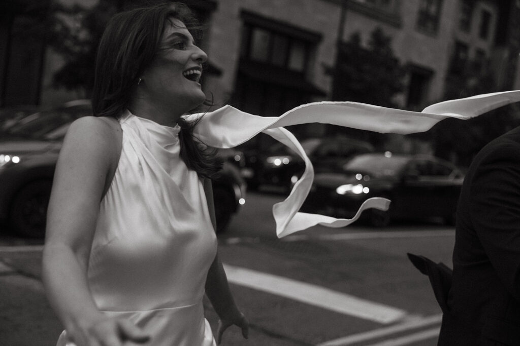 Bride-to-be laughing mid-step in downtown Minneapolis, silk dress flowing in the breeze during candid engagement photos.