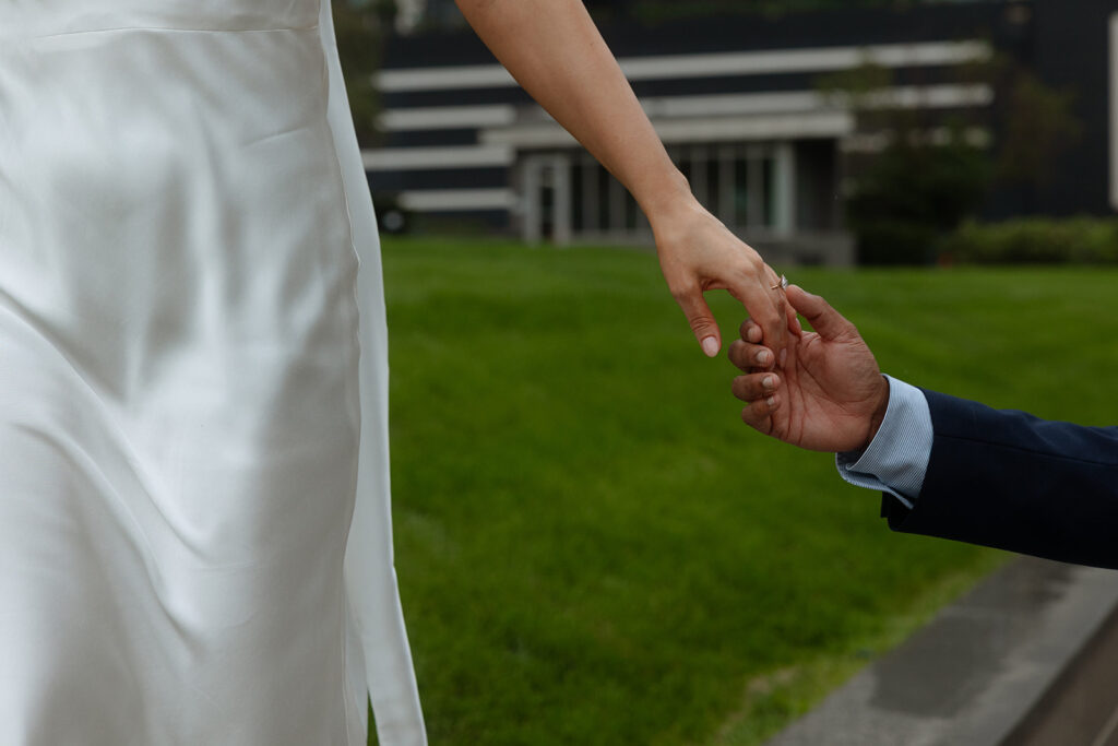 Close-up of couple’s hands linked against a green city backdrop, highlighting modern engagement photography details.