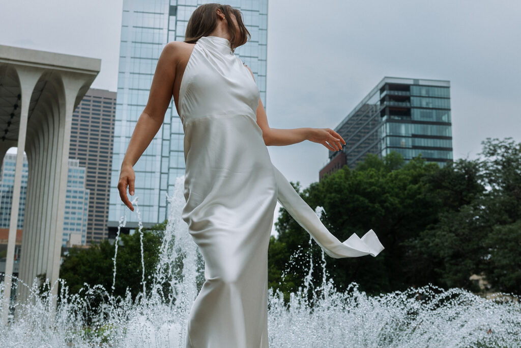 Bride in white gown laughing by the fountain, Minneapolis engagement photography with modern architecture backdrop.