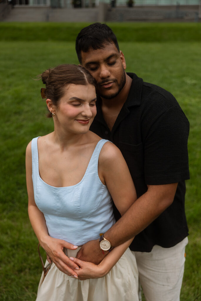 Groom holding bride close in the grass, relaxed and tender outdoor Minneapolis engagement photography portrait.