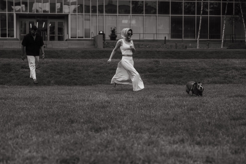 Couple running across a grassy field in Minneapolis with their dog, adding playful energy to their engagement shoot.