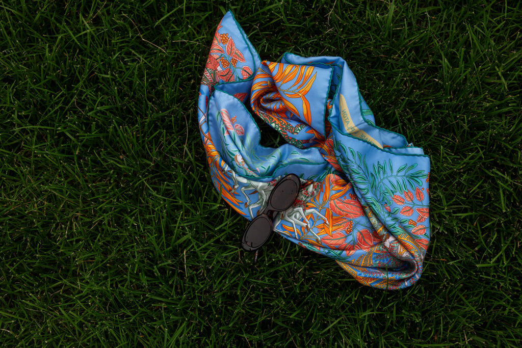 Flat lay of colorful scarf and sunglasses on green grass, editorial detail from Minneapolis engagement photographer.
