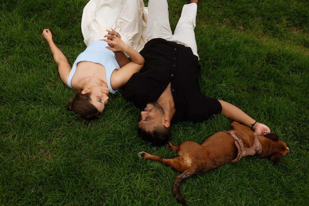 Couple and their dog lying together in the grass, documentary-style engagement photography.