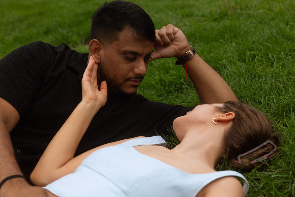 Bride and groom lying in the grass together, soft and intimate engagement photo.
