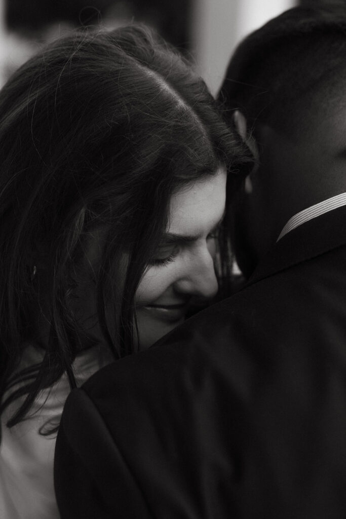 Groom holding fiancée close in black-and-white embrace, candid moment of intimacy.