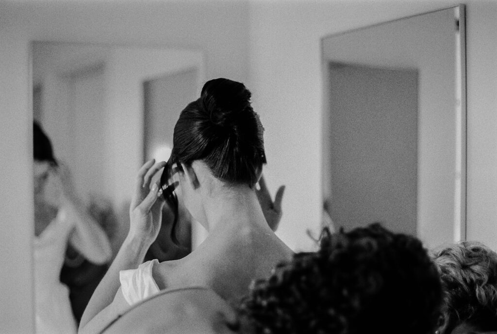 Bride pinning up her hair before the ceremony, surrounded by quiet focus.
