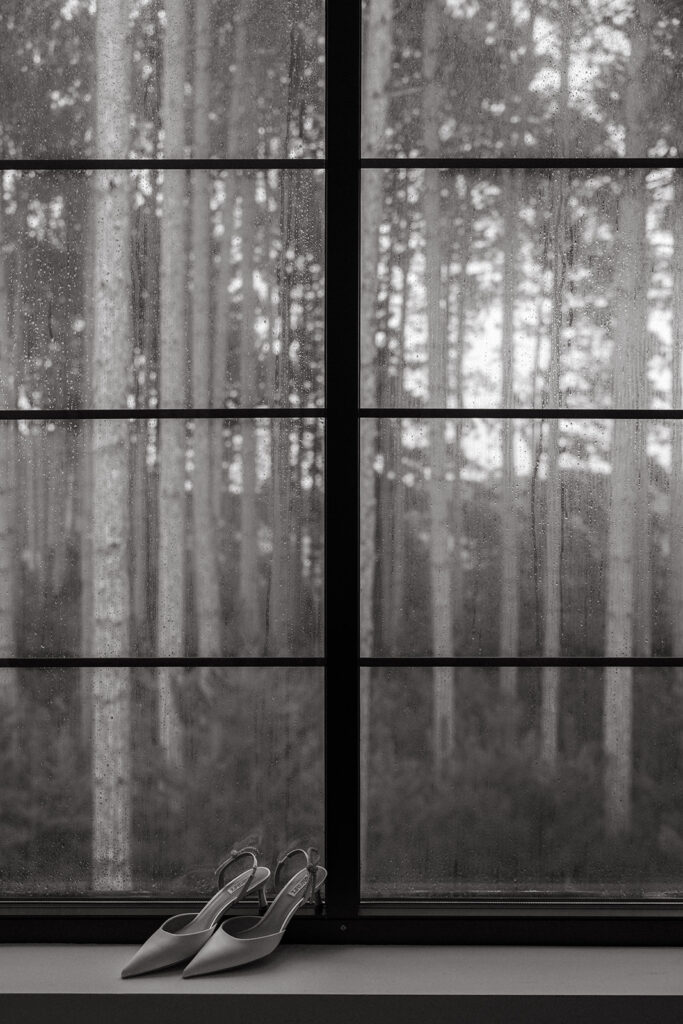 Wedding shoes framed against the window, forest reflection beyond.