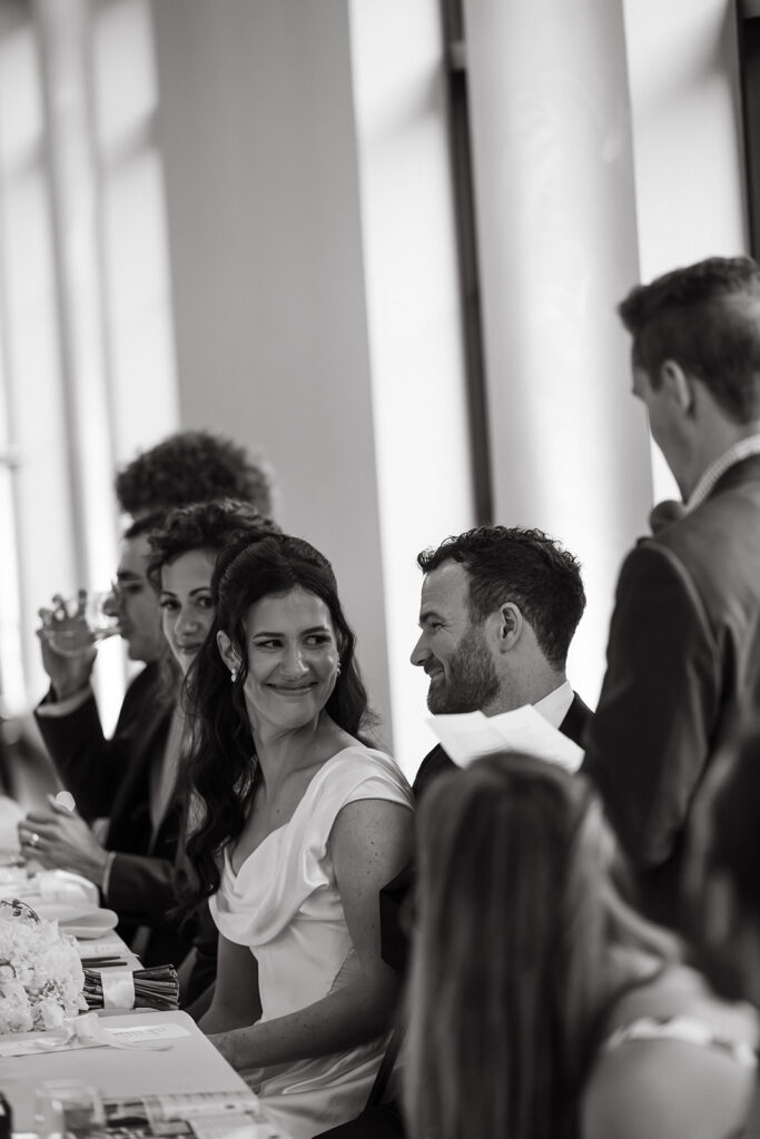 Bride and grim exchange a smile as best man tells story.