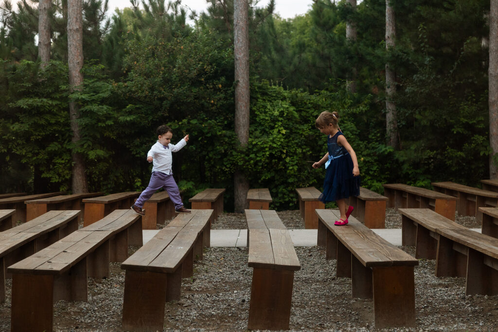 Two kids chase each other between the benches before the ceremony begins, laughter echoing through the woods.