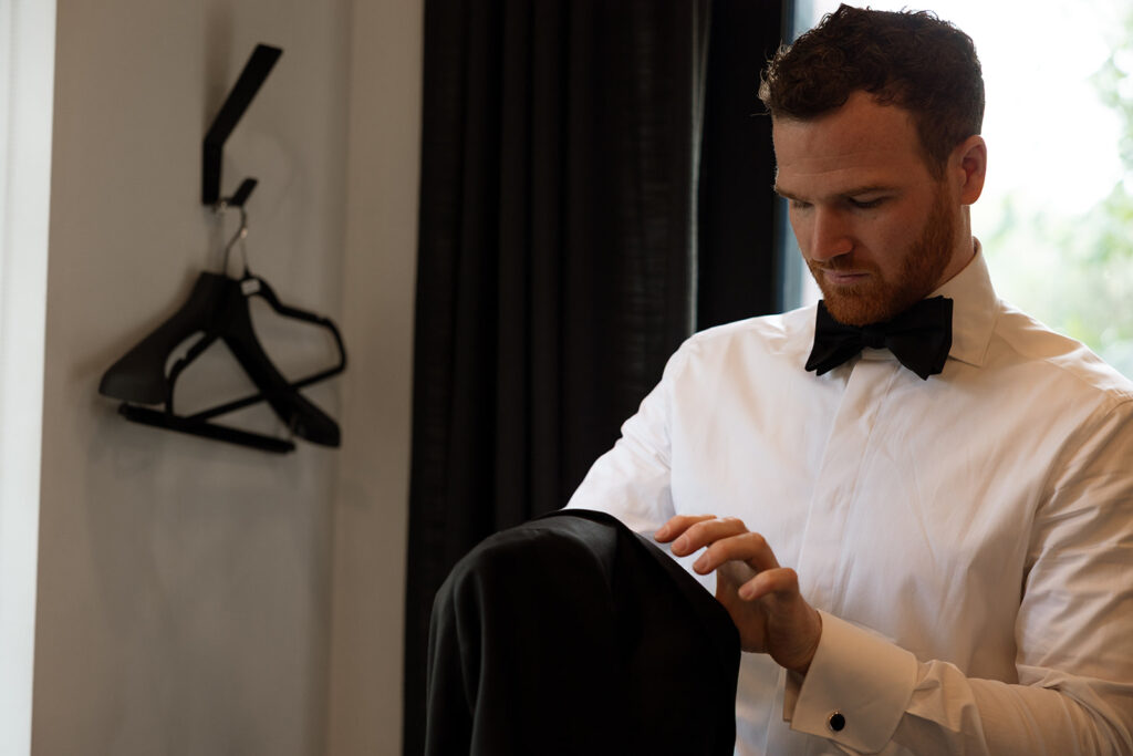Groom slipping into his jacket, morning nerves settling into focus.