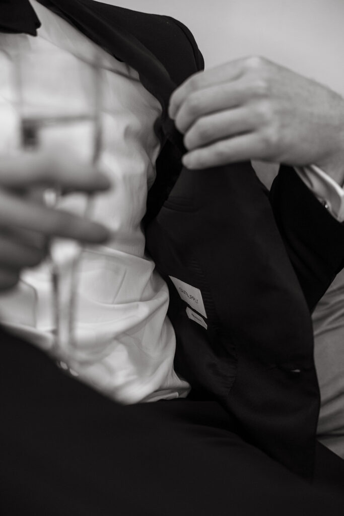 Groom pulling on his tux coat, grin breaking through the quiet in groom portraits.