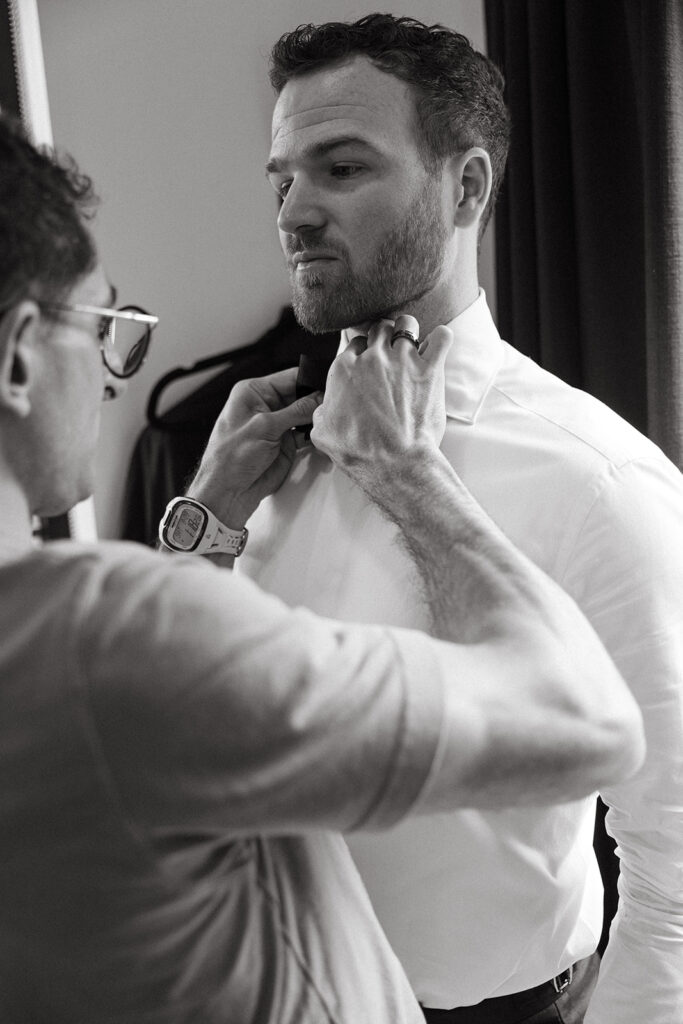 Straightening his tie while his dad helps with the final details.