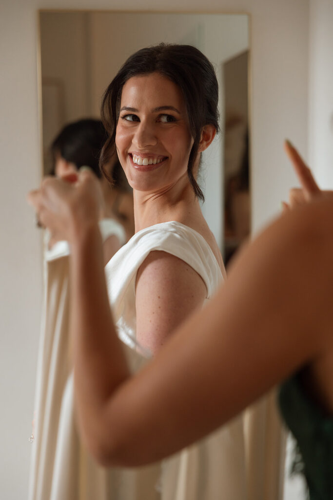 Bride smiling over her shoulder, the calm before the bustle in posed wedding photography that is more unposed than anything.