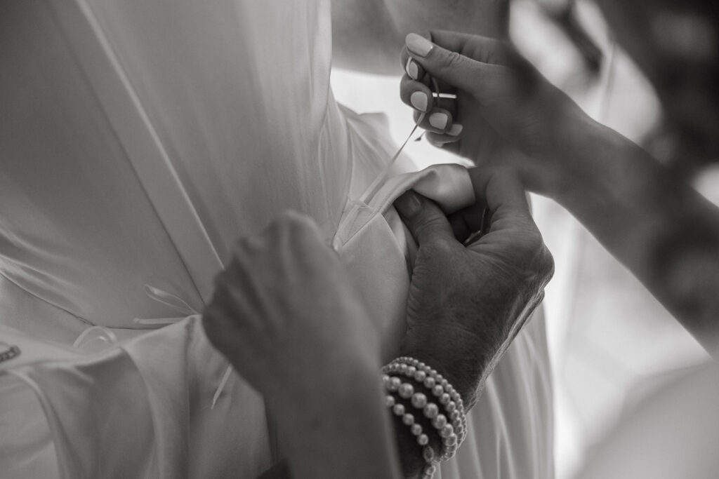 Hands fastening the back of bride's dress, pearls and care intertwined.