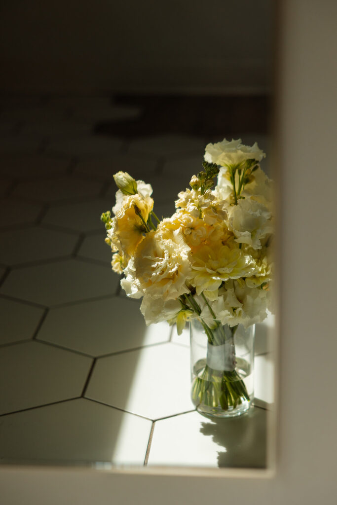 Vase of yellow flowers catching morning light on the tile floor.