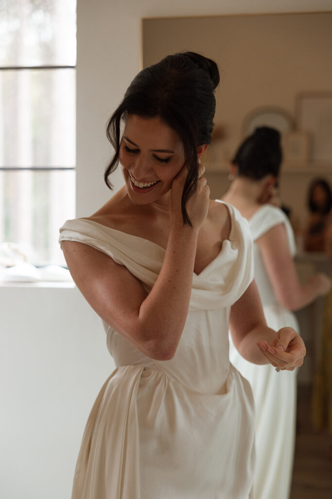 A quiet laugh while adjusting her dress, soft and unposed.