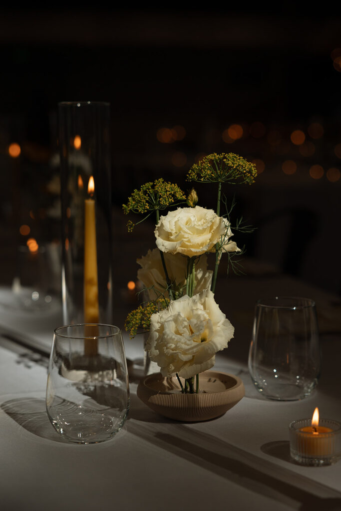 Candlelit reception table with pale blooms and glassware aglow.