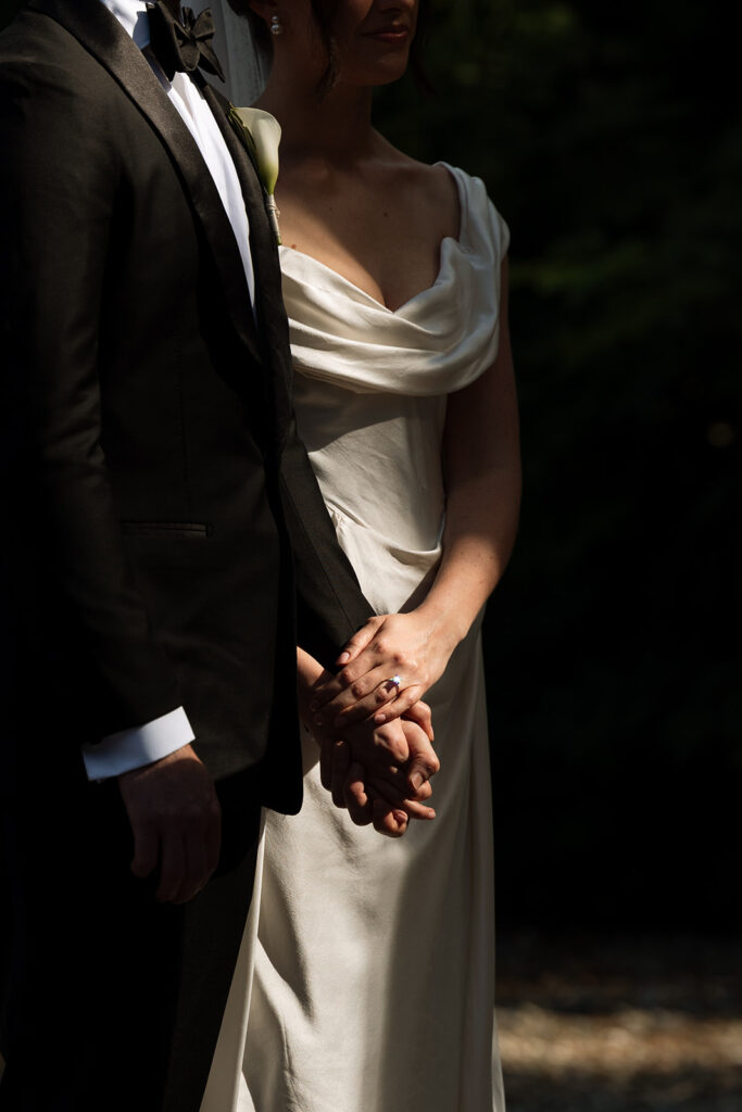 Close-up of bride and groom’s hands and silk folds of her Vivienne Westwood gown—quiet, tactile posed wedding photography.