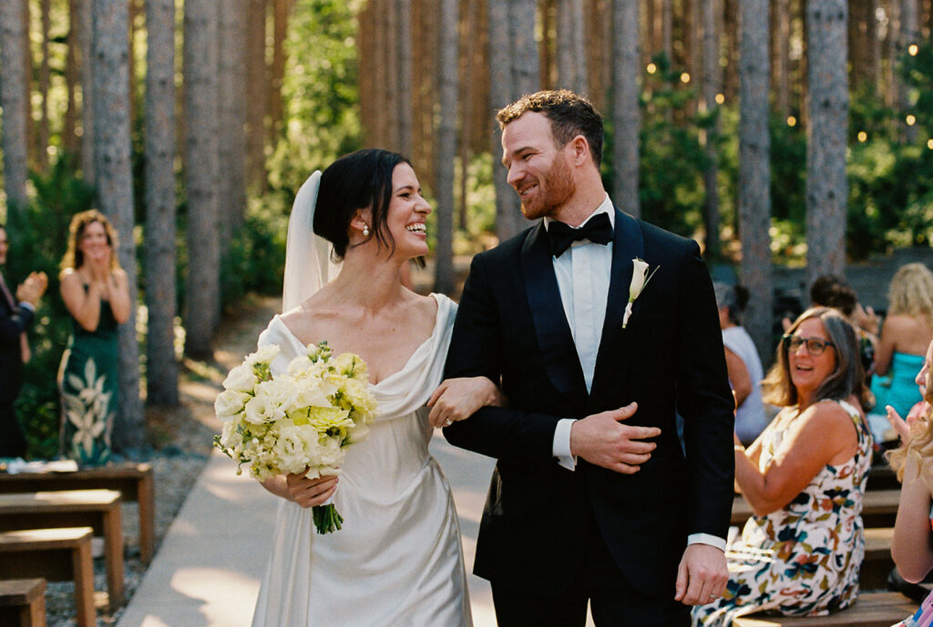 Emma and Isaac walk down the aisle at Pinewood, smiling at each other as their guests applaud.
