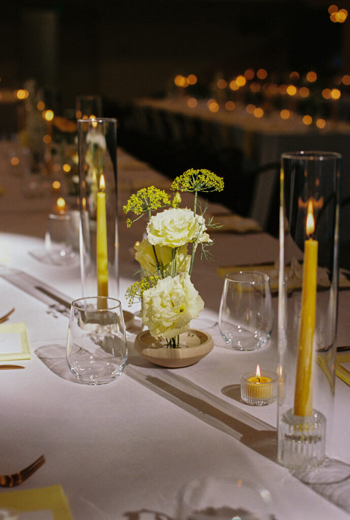 The reception tables glow with candlelight and yellow florals set in minimalist glass vases.