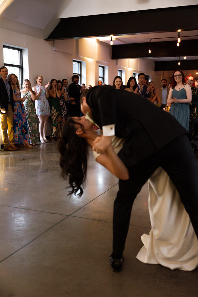 Emma and Isaac share their first dance surrounded by cheering friends, a perfect blur of light and movement in posed wedding photography.