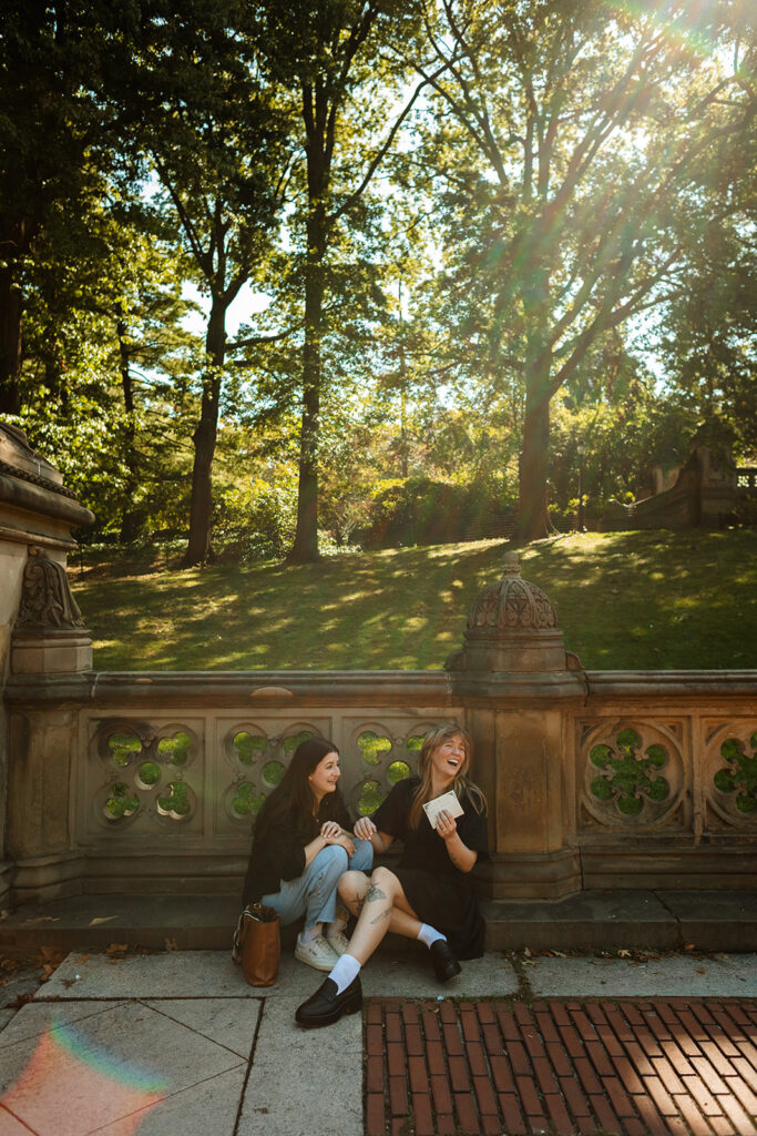 Sunlight streams through the trees as a queer couple reads their handwritten proposal letters on the Bethesda Terrace wall during their emotional New York City wedding proposal.