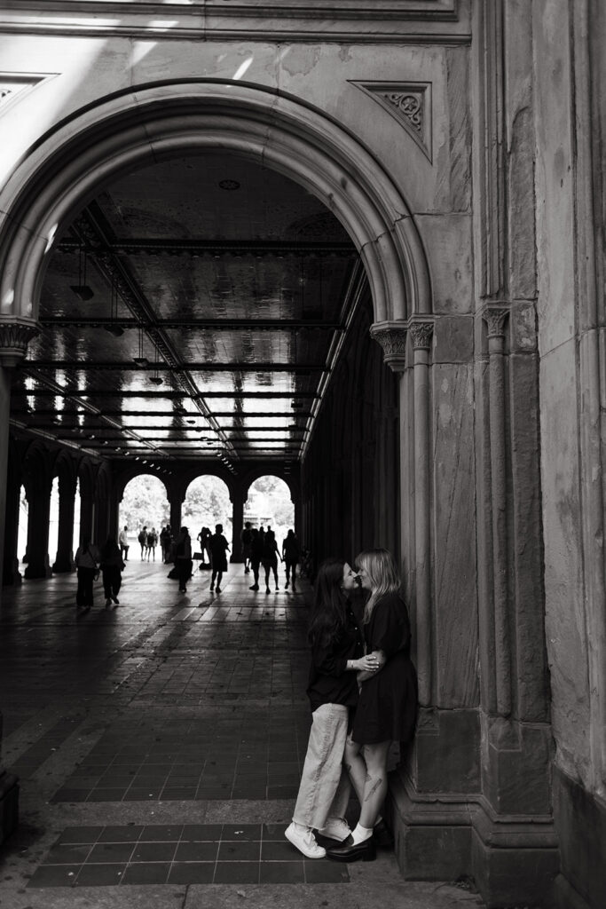 A couple shares a quiet kiss beneath the dramatic arches of Bethesda Terrace, silhouetted by light during their NYC documentary-style proposal photos.