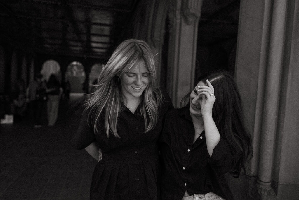 A black-and-white photo of a couple walking through the Bethesda Terrace arcade, laughing as they hold each other after their Central Park proposal.