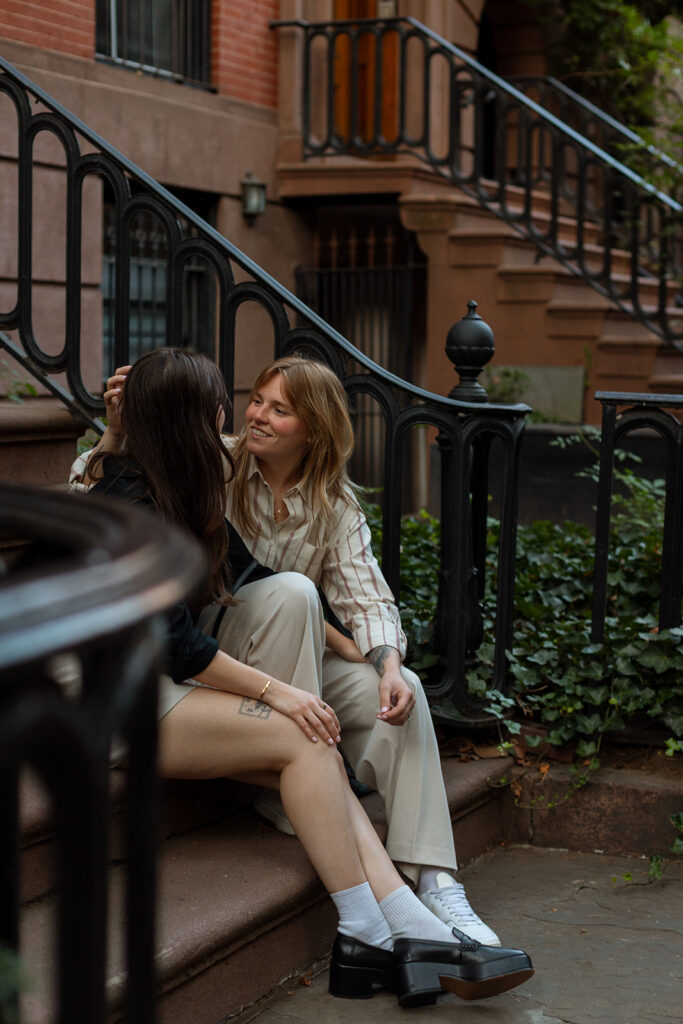 A couple sits close on brownstone steps in Manhattan, tucked into each other with quiet smiles during their NYC engagement photoshoot.