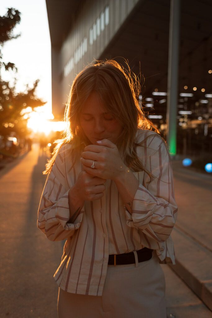One partner shields a lighter from the wind as she lights a joint at sunset in Manhattan, golden light spilling across the sidewalk during their candid NYC photoshoot.