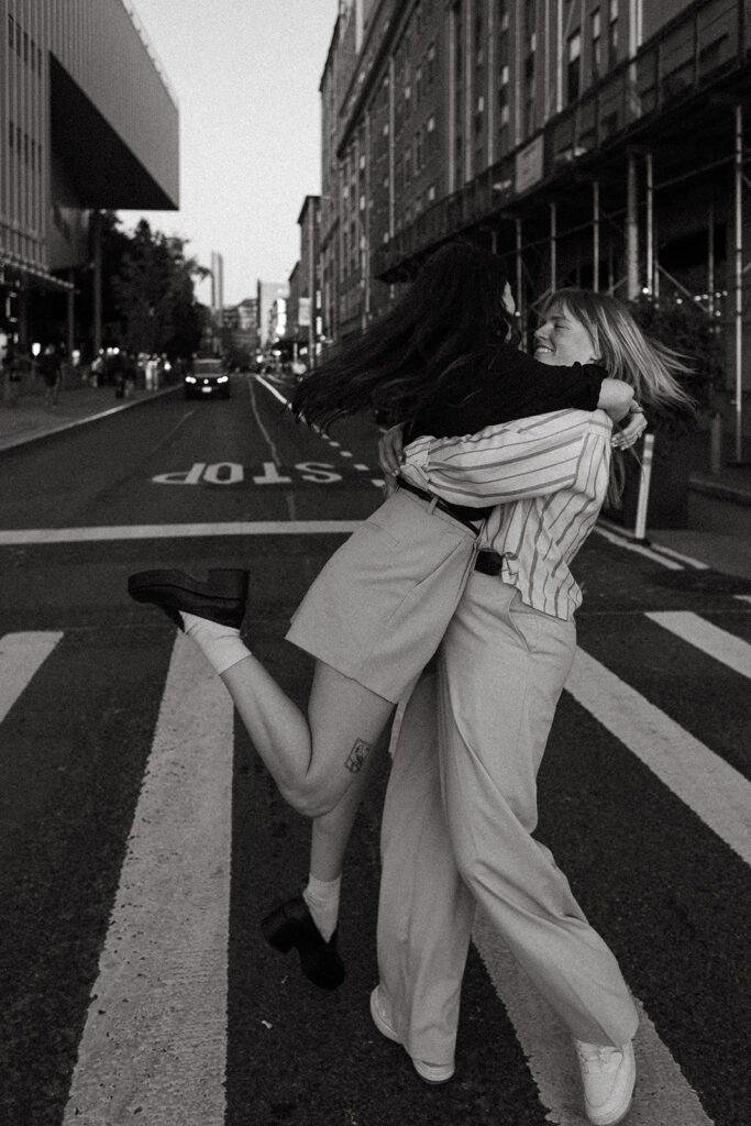 A joyful couple spins each other in the middle of a New York City street, captured mid-twirl in a candid, documentary-style engagement photo.
