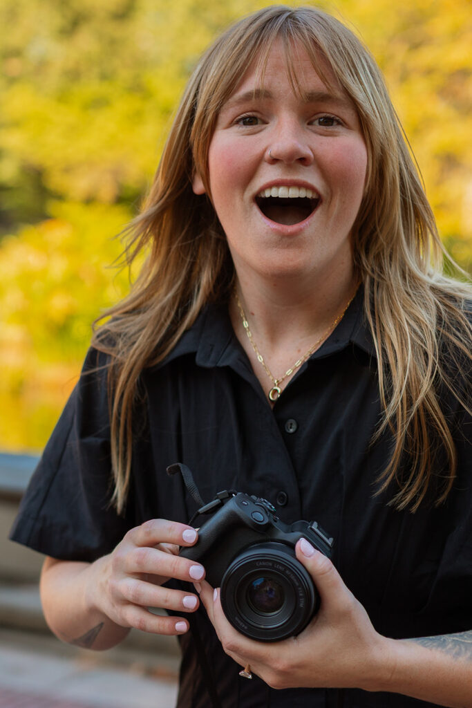A woman reacts with joyful disbelief while holding a camera, moments after her partner proposes during their NYC engagement at Bethesda Terrace.