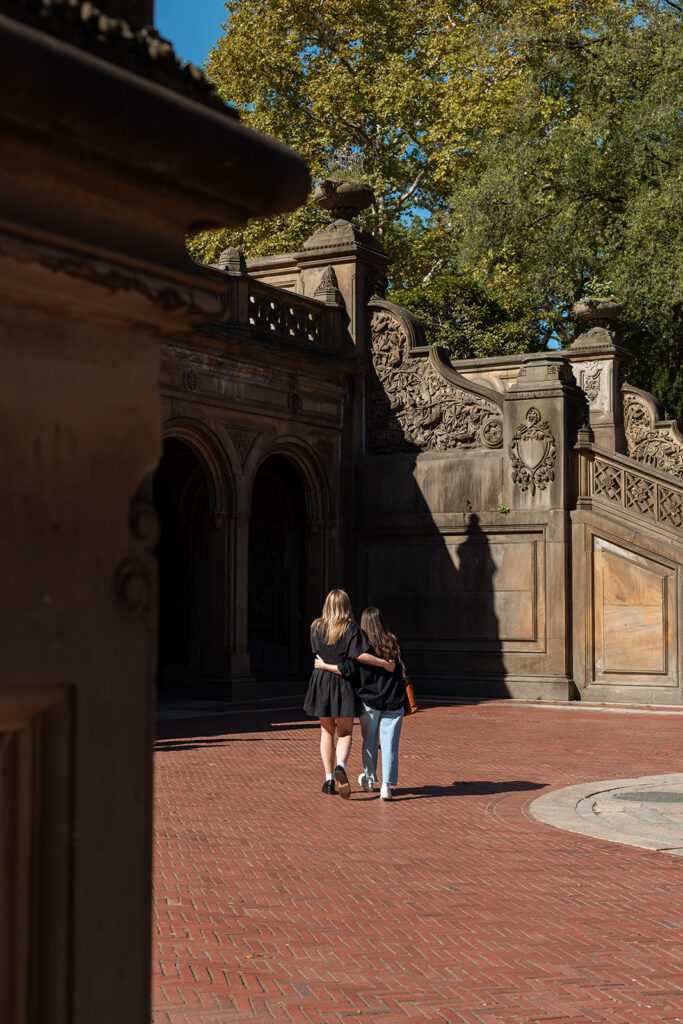 A queer couple walks hand in hand toward the ornate arches of Bethesda Terrace in Central Park during their New York City proposal session.