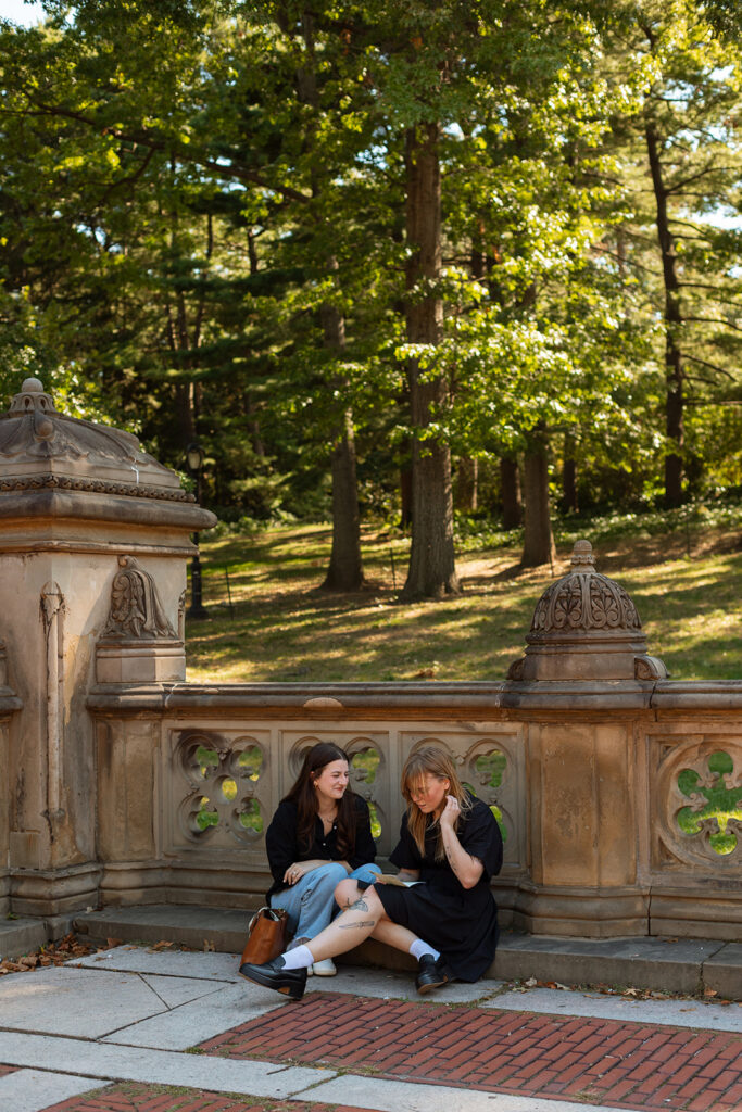 A couple sits on the carved stone wall of Bethesda Terrace, eagerly reading handwritten proposal letters under the afternoon sun in Central Park.