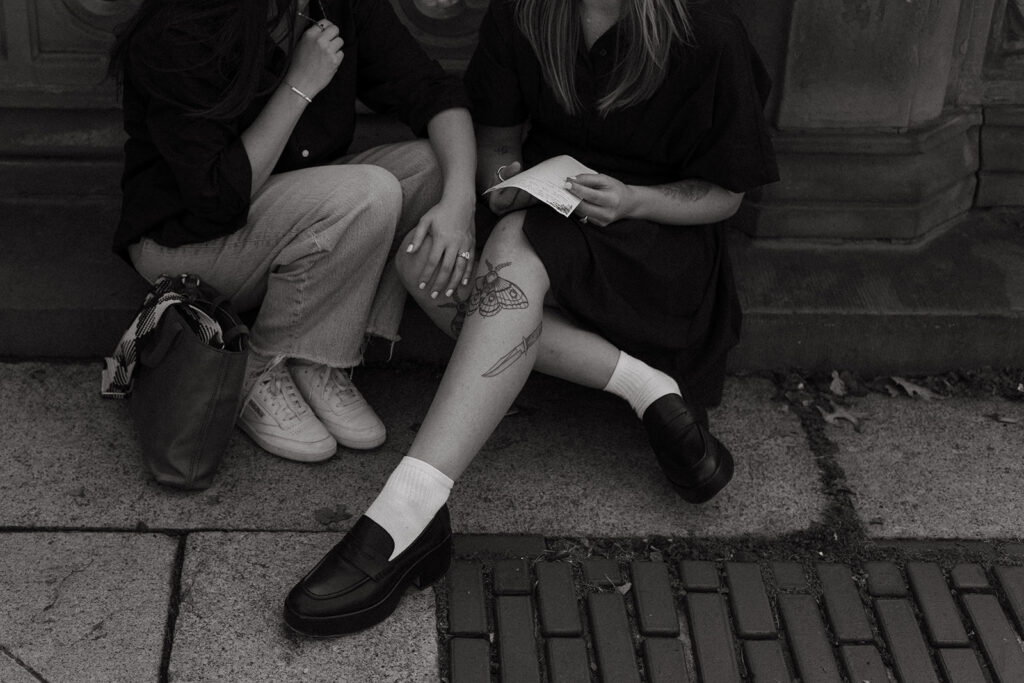 A black-and-white close-up of a couple sitting on the ground in Central Park, hands intertwined as one partner holds a handwritten letter during their emotional New York proposal.