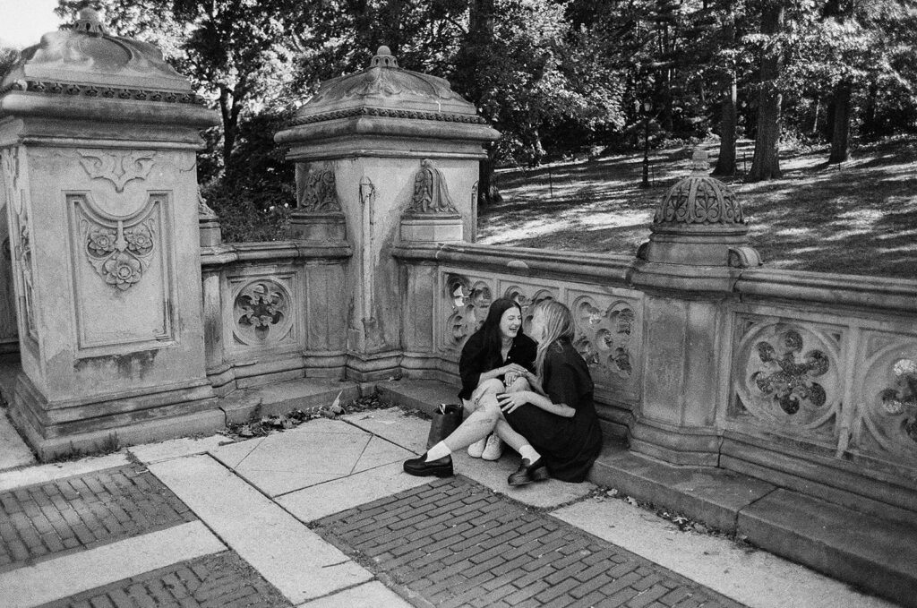 A black-and-white image of a couple sitting close on the Bethesda Terrace wall, sharing letters and quiet emotion during their NYC proposal photos.