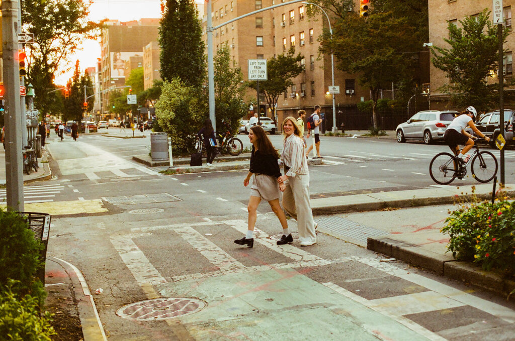 A couple moves through a busy Manhattan crosswalk at sunset, the golden light hitting their backs during their candid engagement session.